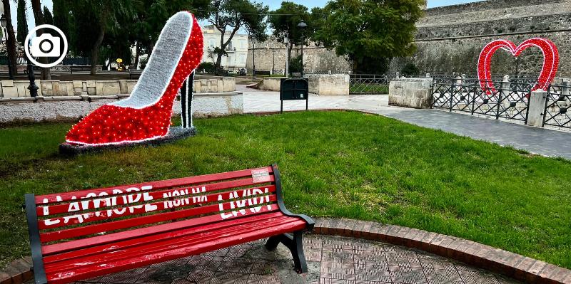 Affianco a panchina rossa, luminaria di una scarpa rossa con tacchi. Simboli contrasto a violenza sulle donne